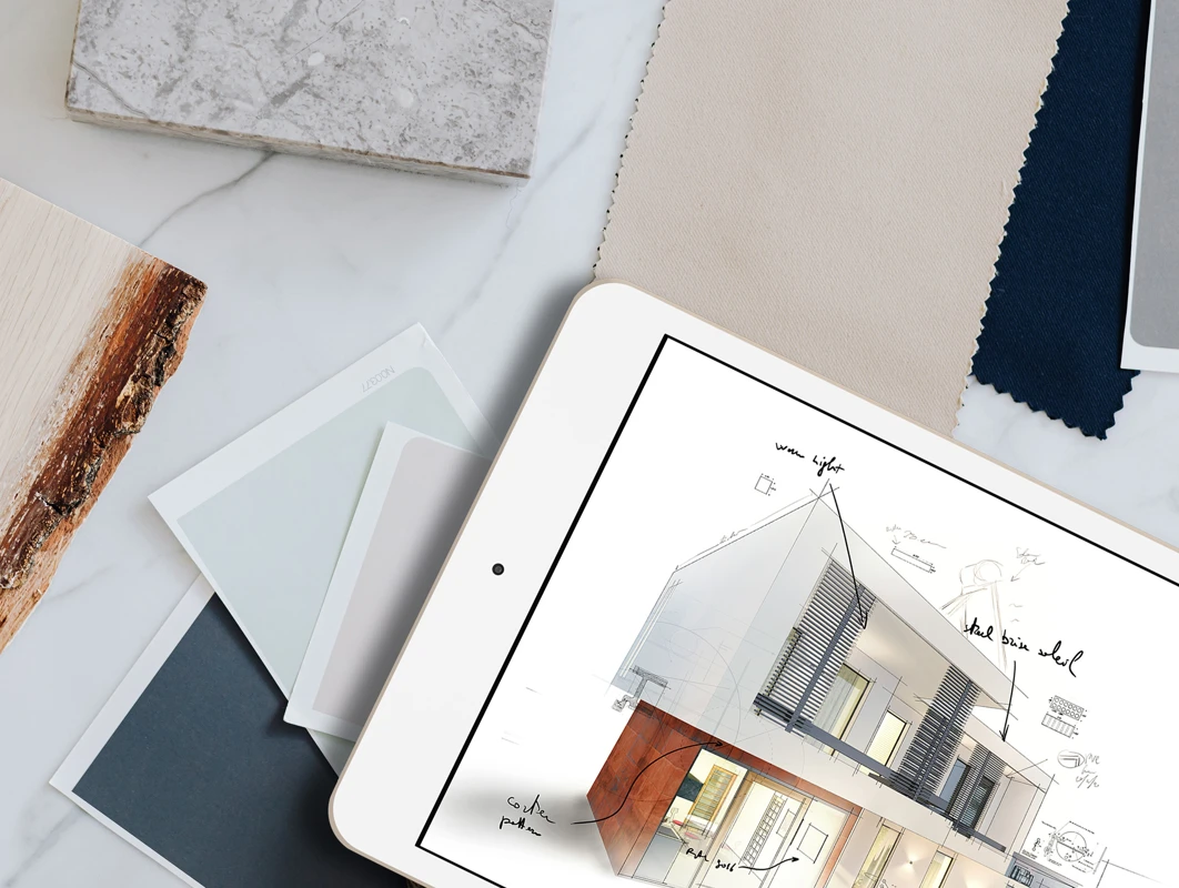 Tegninger av moderne husdesign på et nettbrett, omgitt av fargeprøver og tekstilprøver på et marmorbord