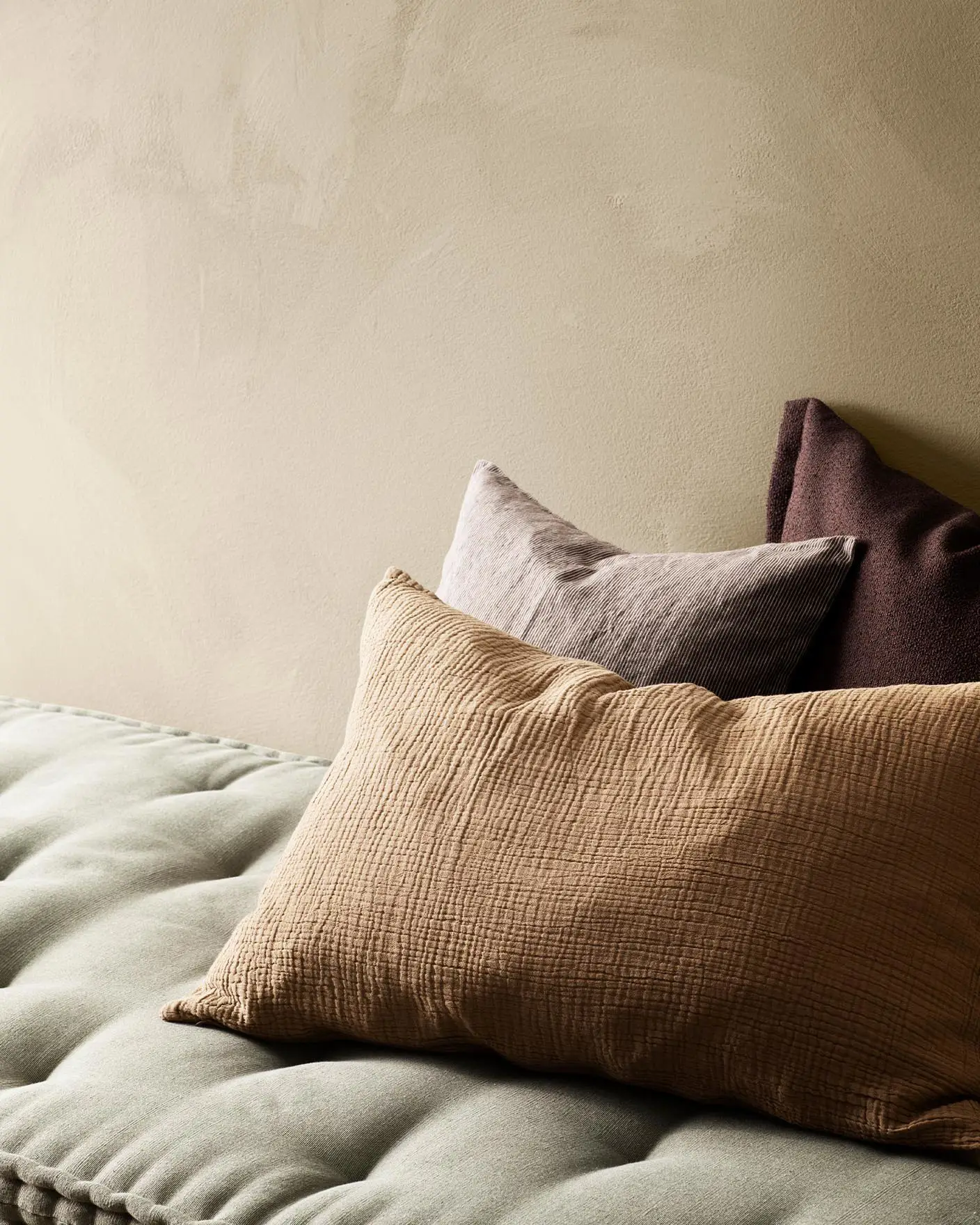 Dempede jordfargede puter på et mykt grønt sete, mot en varm, brunaktig, gylden vegg malt med LADY Minerals og fargen Jotun 1303 Observe.