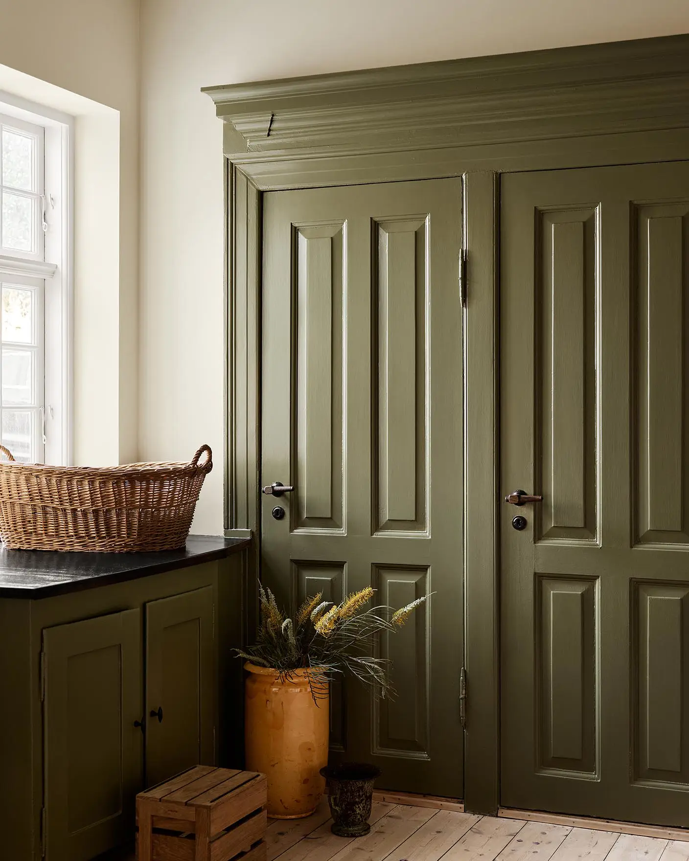 Kitchen with olive-green cabinets in the colour 8597 Seaweed Green against a muted yellow wall painted with 12079 Gleam from Jotun.
