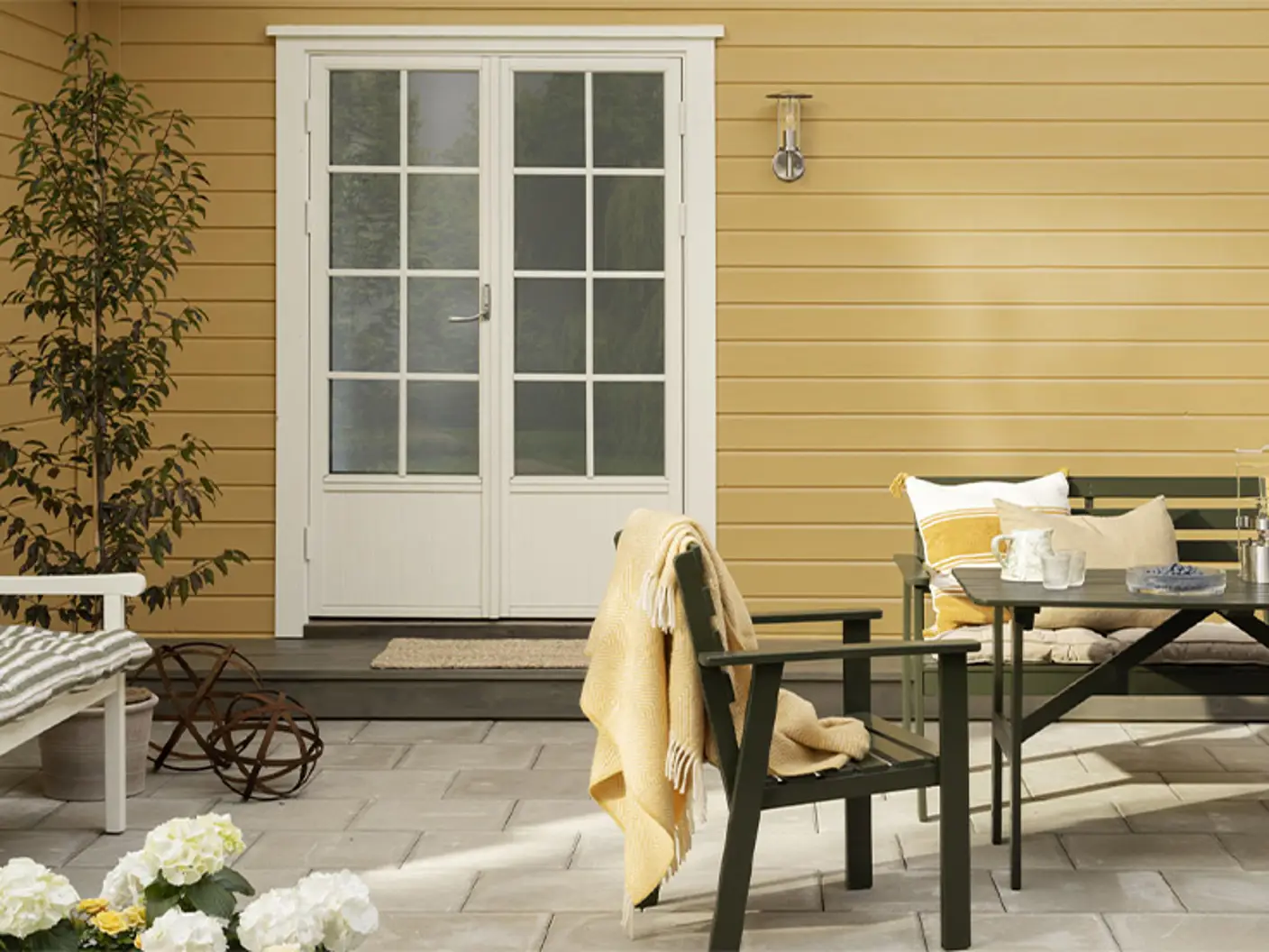 Jotun husmaling i fargen Skagengul i solfylt uteområde med møbler malt i Grønn Umbra