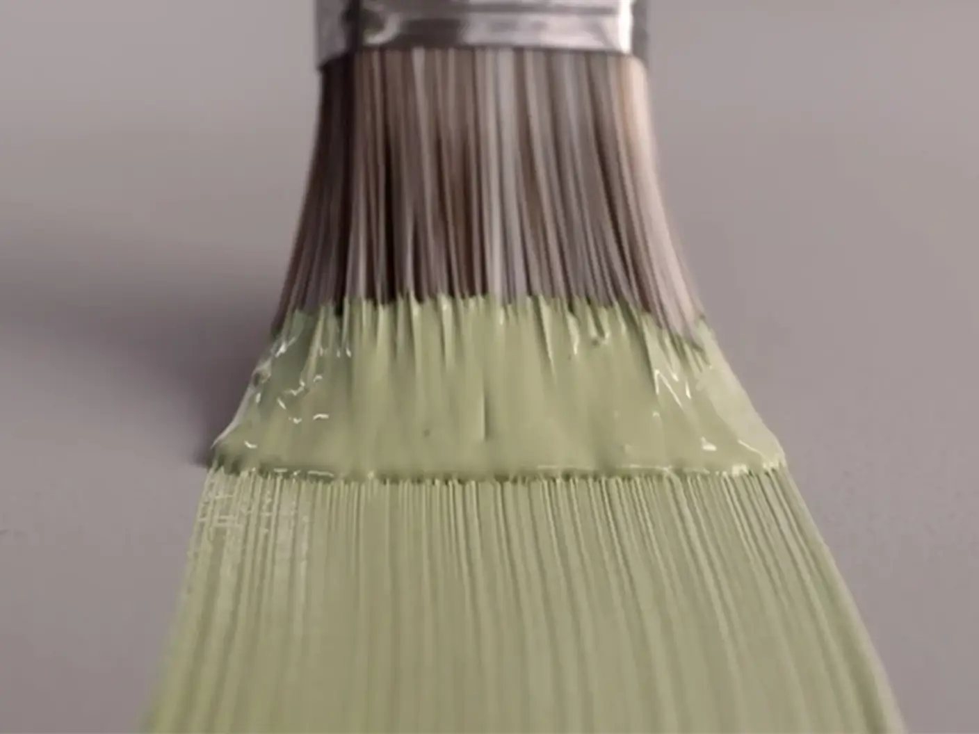 Pensel med lys grønn maling stryker malingen utover en grålilla flate