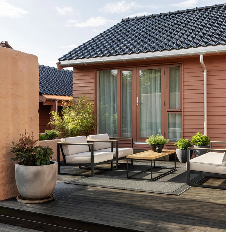 Modernt uteplatsområde med sittgrupp och rottingmöbler utanför ett hus med träfasad och tegeltak i Sverige. Fasad målad i Jotun 20118 Amber Red.
