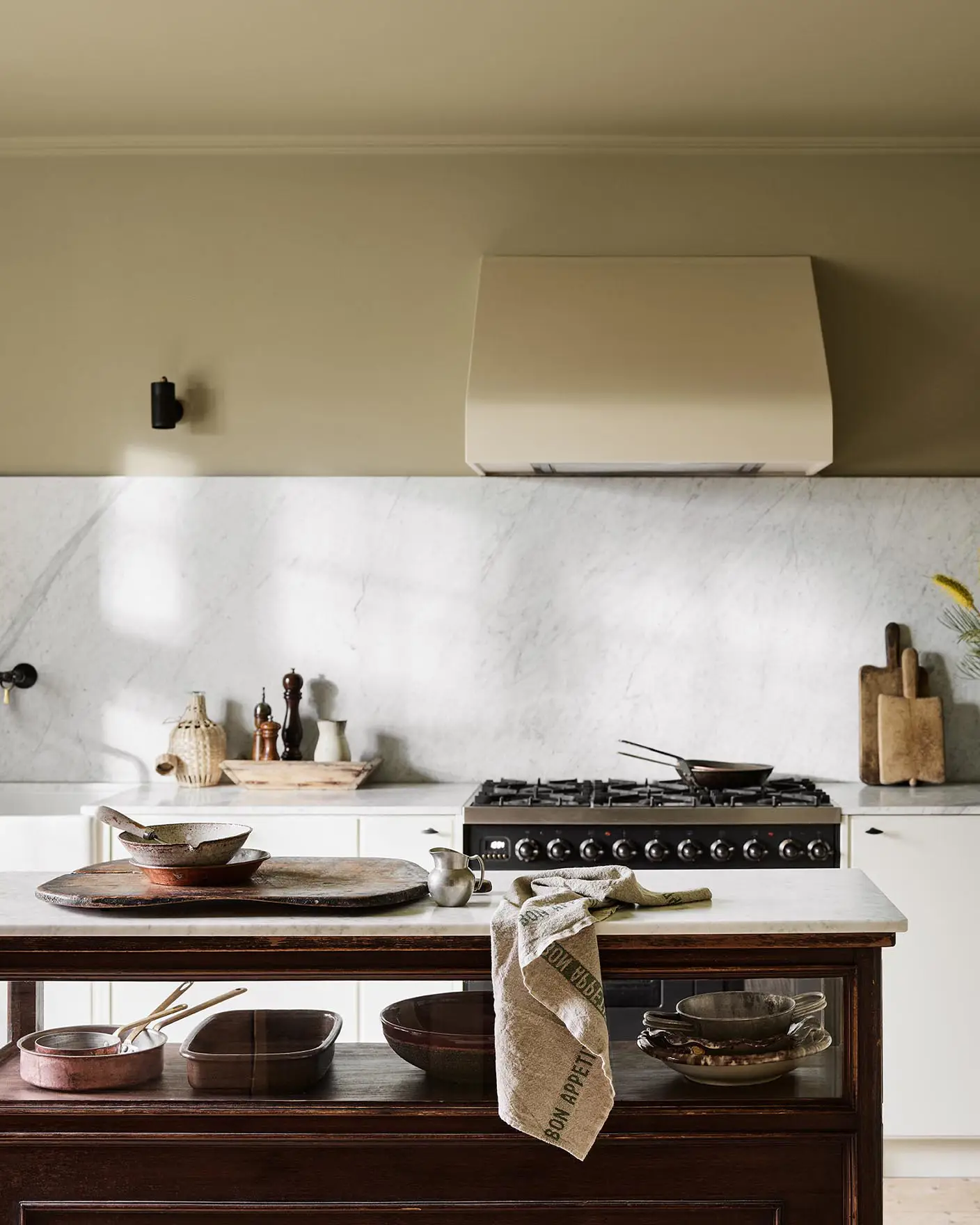 Kitchen with a marble backsplash, white cabinets, and a wooden island. Wall painted with the Jotun colour 8284 Olive.