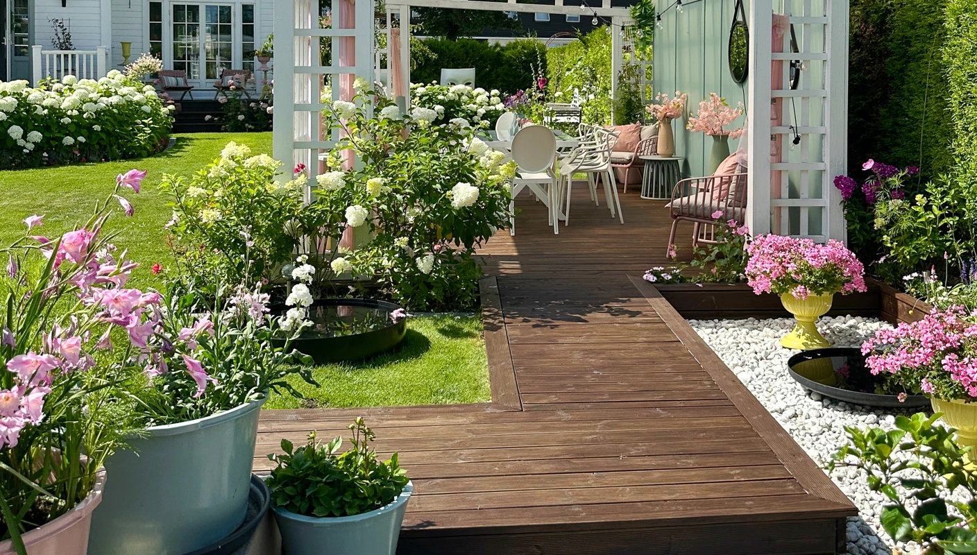 Brunt terrassegulv beiset med TREBITT Terrassebeis i Terrassebrun, ute i en grønn hage med en pergola malt hvit med JOTUN Klassisk Hvit
