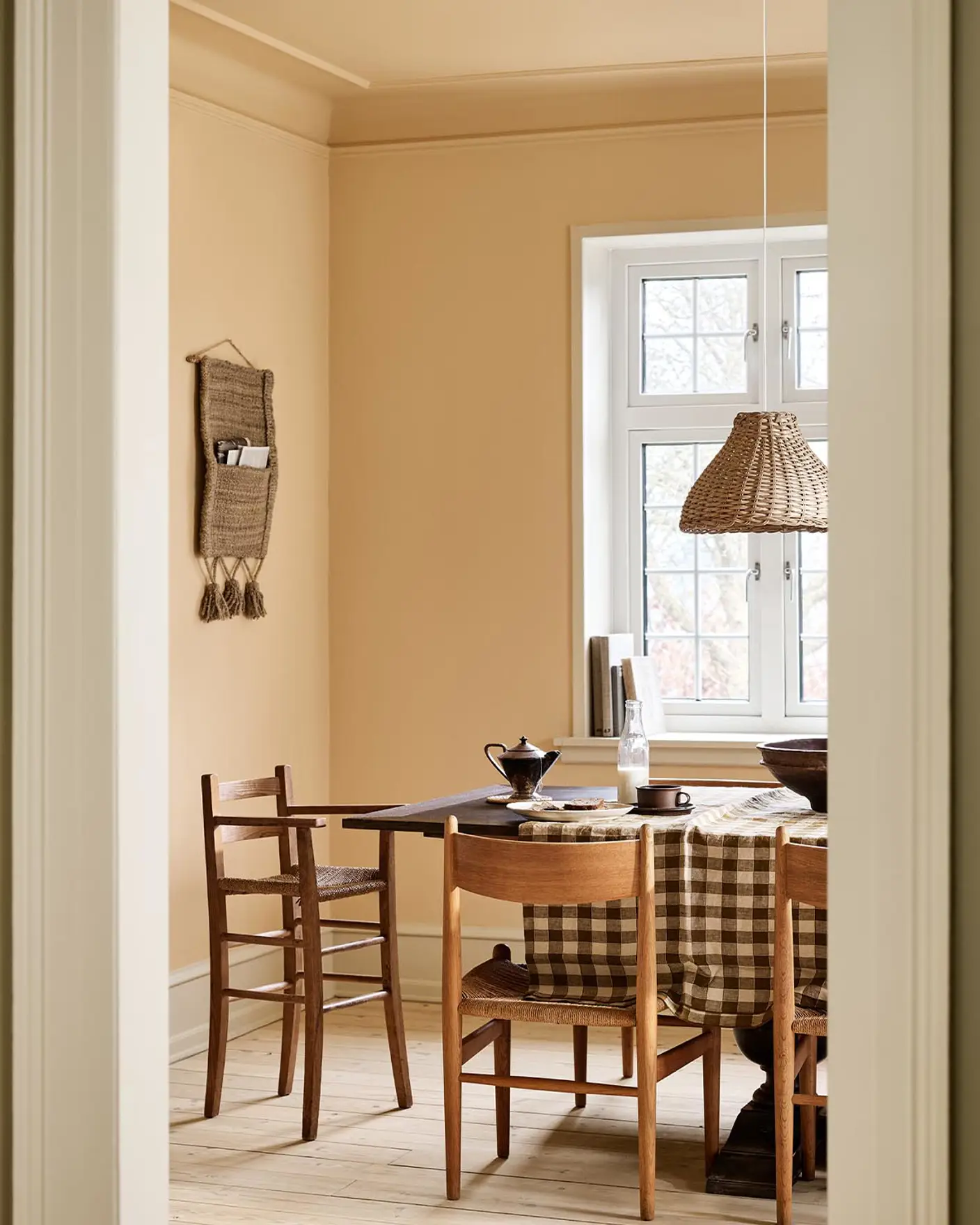 Dining area with a checkered tablecloth, wooden chairs, and ochre coloured walls and ceiling painted with Jotun's 11202 Mild Ochre.