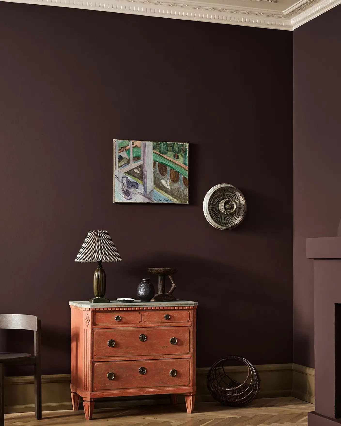 A red dresser, wall art, and fireplace against a deep, brownish red wall painted with the colour Jotun 2149 Coffee.