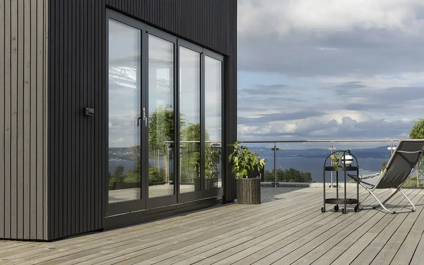 Moderne utendørs terrasse med tregulv beiset med TREBITT Terrassebeis i fargen 90029 Naturlig Sølvgrå, glassrekkverk og lenestol med utsikt over et naturskjønt landskap under en skyet himmel