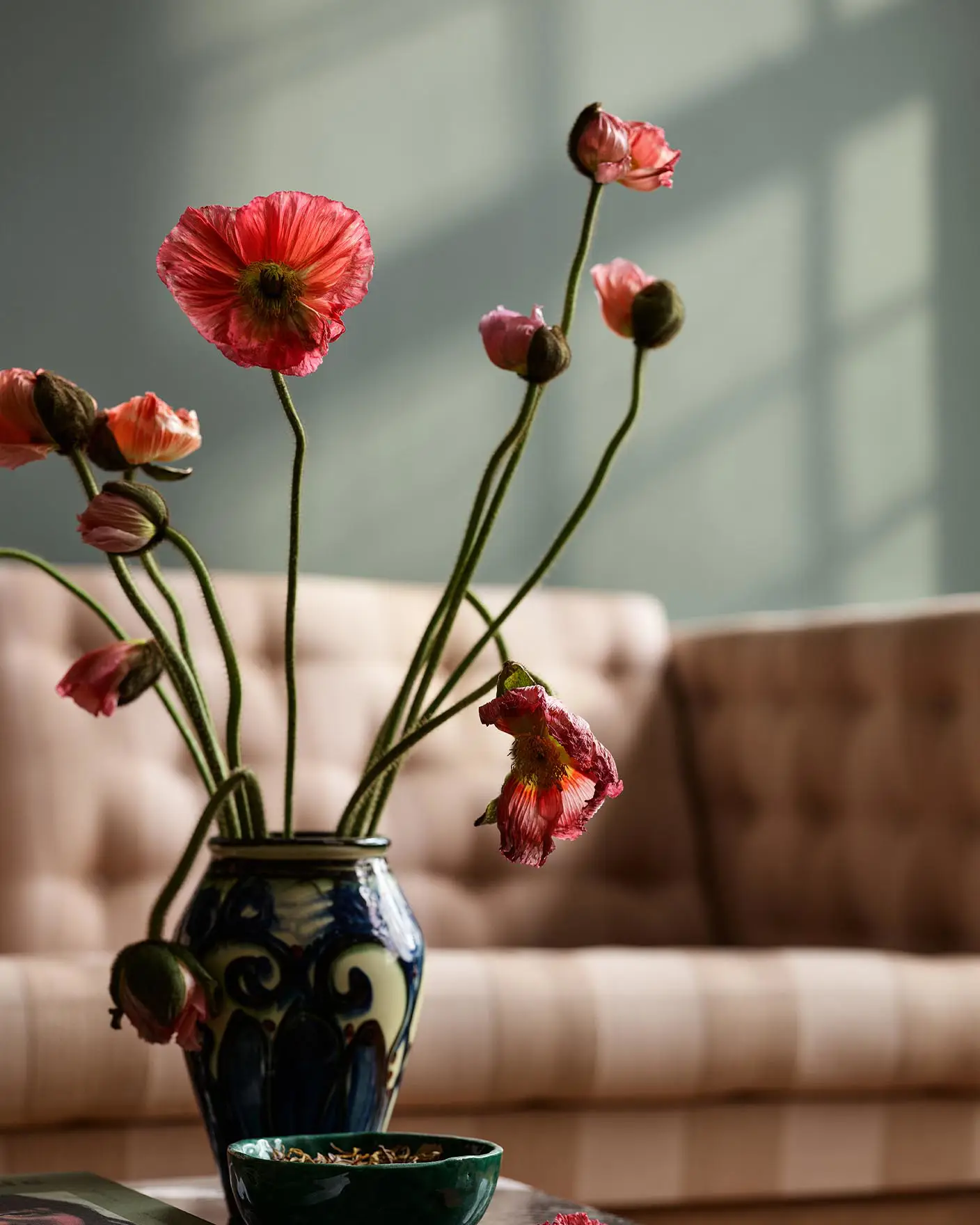 Vase with pink and red flowers on a table in front of a beige sofa. Background wall in the muted green colour Jotun 7613 Northern Mystic.