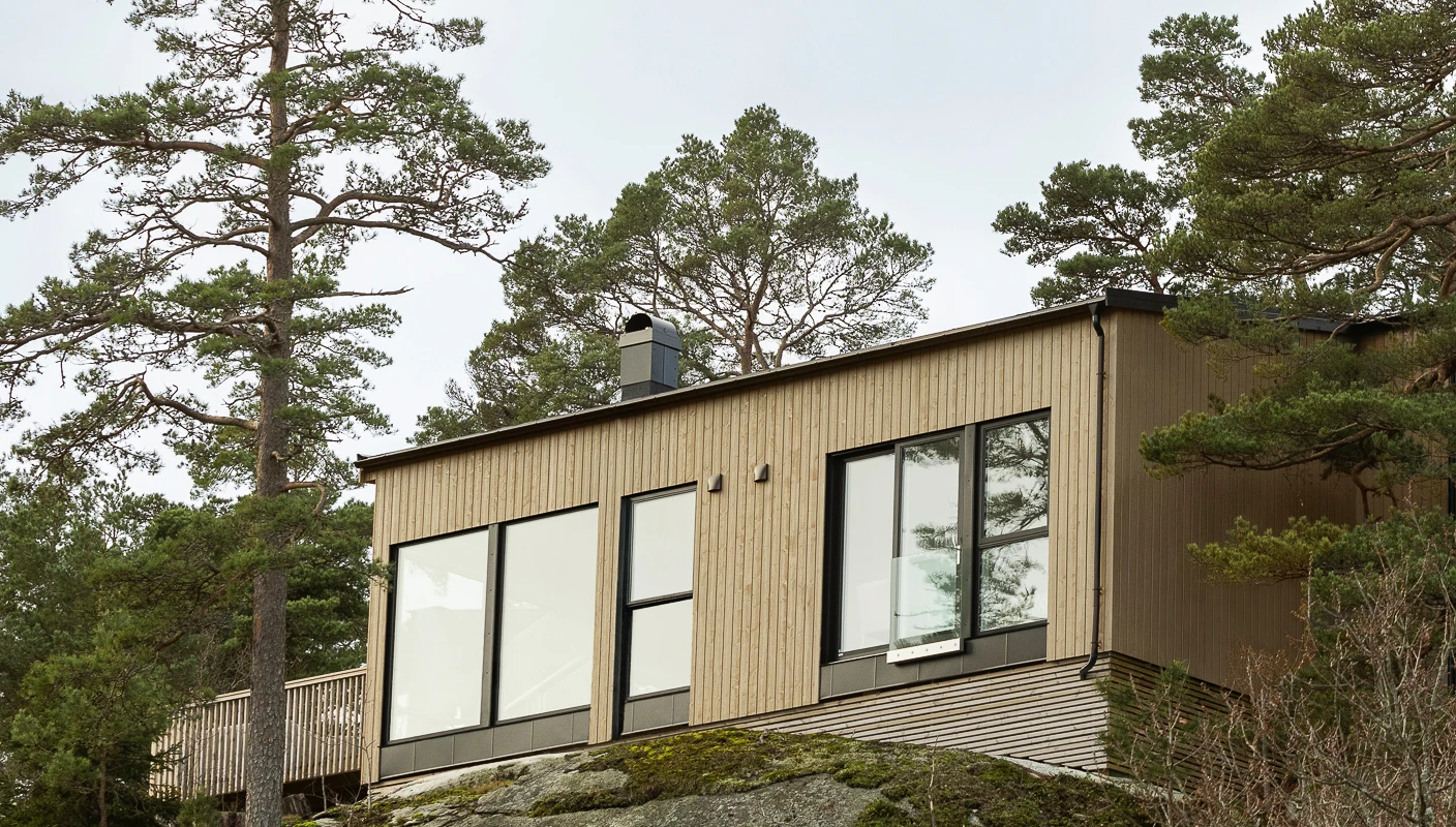 Hytte på fjell omkranset av furutrær. Kledning i tre beiset i to farger, gulbeige og sort med Jotun TREBITT Naturlig Eldet og Funkissort.